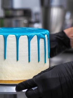 A pastry chef applying blue icing on a white cake, highlighting the baking process in a kitchen