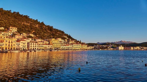 The setting sun bathes the coastal town in a warm light with reflections in the water, Taygetos