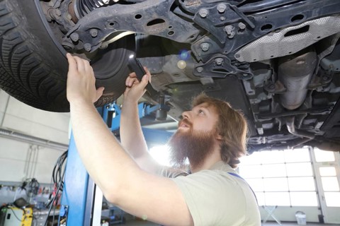 Symbolic image: Motor vehicle mechatronics technician inspects a car on the lift