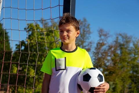 Symbolic image: Ten-year-old boy on a football pitch proudly holding a football in his arms