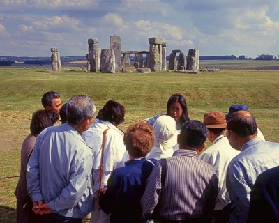 Group of Japanese tourists with guide visiting Stonehenge monument at Salisbury, England, UK,