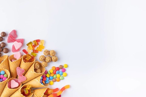 Colourful sweets, gummy bears, chocolate lentils falling out of ice cream cones, copy room, white