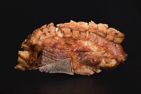 Freshly roasted pork belly with bone and crispy crust, food photography with black background