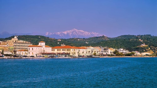 Coastal city view with buildings in front of a mountain backdrop under a clear blue sky,