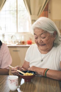 Portrait of an elderly Japanese woman with gray hair eating rice with chopsticks. Vertical portrait