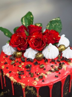 A cake decorated with red glaze, red roses, and chocolate pieces