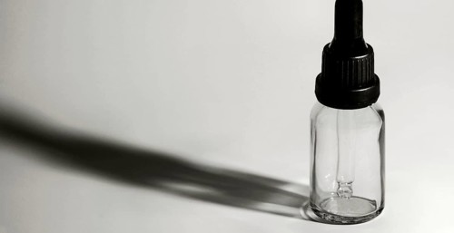 Closeup of single eye dropper bottle with strong dark shadow on white background