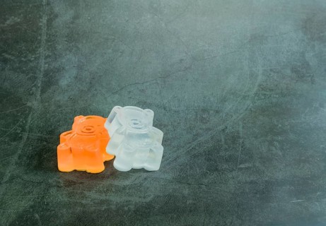 One orange, one white homemade bar of soap made to resemble toy bear on black textured background