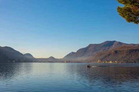 Boat Travel on Lake Lugano with Mountain and City in a Sunny Day with Clear Sky in Porto Ceresio,