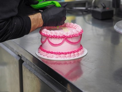 Decorating with text mesagge the top of pink cake with intricate icing patterns using a pastry