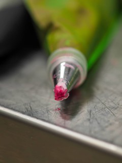 Close-up of a piping pastry bag tip with a bit of pink icing on it, resting on a metal surface