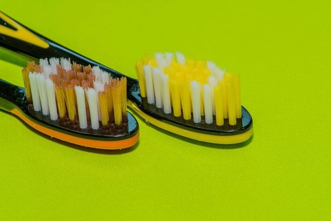 Closeup of two toothbrushes in orange and yellow on a green background
