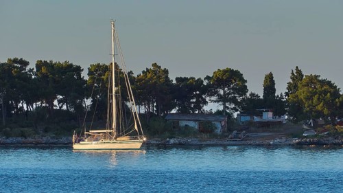 A sailing boat floats at dawn near the coast with trees, Gythio, Mani, Peloponnese, Greece, Europe