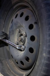 Vertical detail of an unrecognizable mechanic loosening lug nuts to change a flat tire on a vehicle