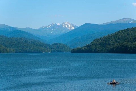 A small boat on a calm blue reservoir with snow-capped mountains in the background, Vidraru