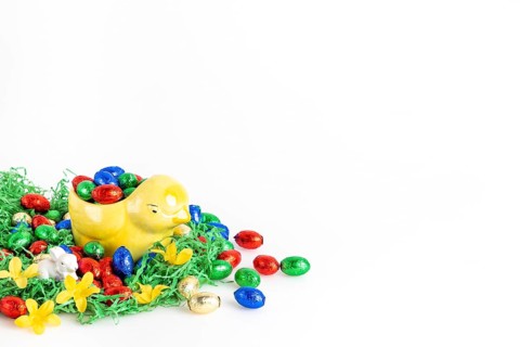 Chocolate eggs and a decorative chick surrounded by artificial grass as a festive decoration, white