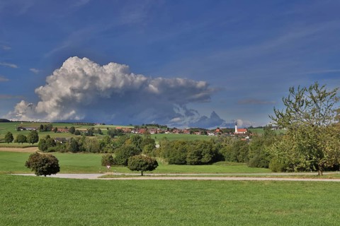 Threatening thundercloud over a sunny, hilly landscape with a village in the foothills of the Alps,