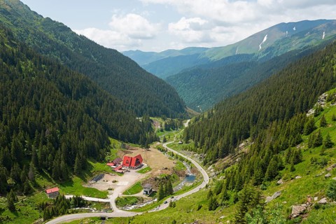 A green mountain valley with a river and a road, surrounded by dense forests, mountain road, Capra