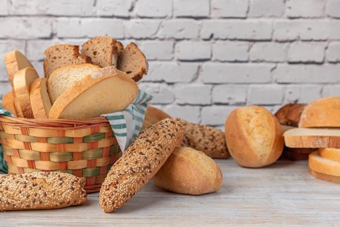 A woven bread basket filled with a selection of bread on a wooden table