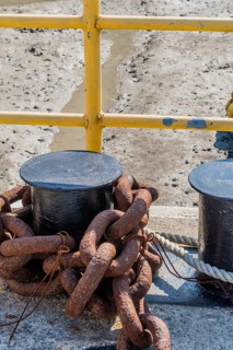 Rusty chain wrapped around ships mooring post in front of yellow metal fence in Yeosu, South Korea,