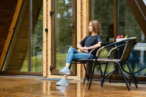 Cute woman enjoys fresh air after the rain sitting on terrace of her forest cabin