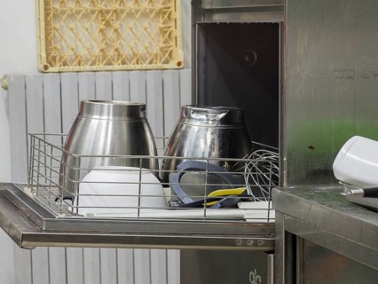 An assortment of metal kitchenware lying on a dish washer in an industrial kitchen