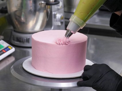 Close-up of a confectioner's piping bag adding pink frosting to decorate a cake with swirls,
