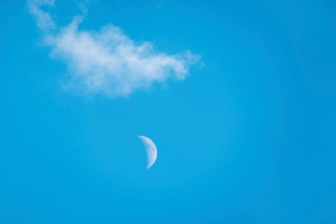 The crescent of the waxing moon in the second quarter shines during the day in a clear blue sky