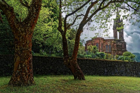 Hidden Gothic church Capela de Nossa Senhora das Vitorias behind trees and an old stone wall in a