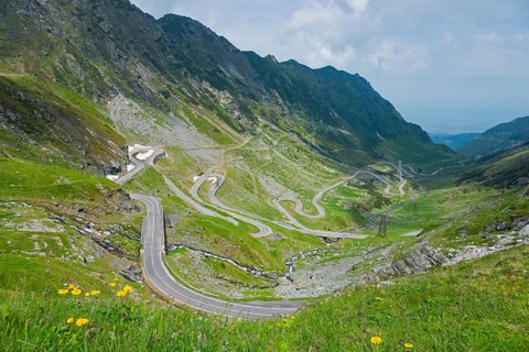 A winding mountain road meanders through a green landscape on a cloudy summer day, Mountain Road,