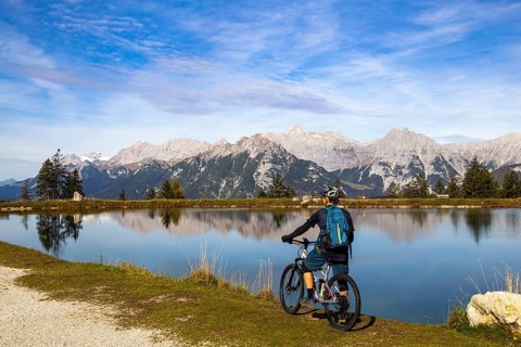 Mountain biker taking a break at the Kaltwassersee lake in Seefeld/Tyrol. The snow-covered peak on