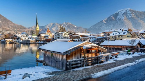 Snowy winter view of Malerwinkel with boathouses, parish church and Wallberg 1722m, Rottach-Egern,