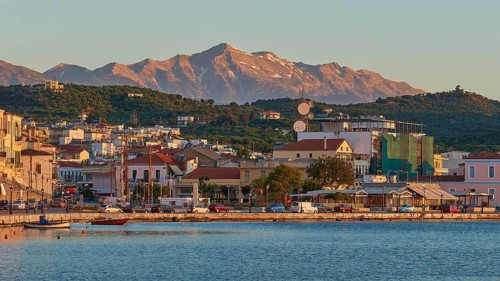 Evening sun illuminates a picturesque harbour town by the sea with mountains in the background,