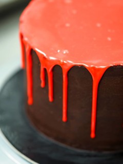 A chocolate cake with red dripping icing on a black surface, creating a sense of celebration