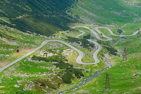 A serpentine road winds through the mountain landscape with views of electricity pylons, Balea