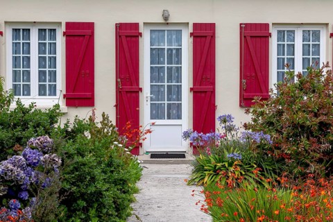 House facade with mullioned windows, entrance door, red shutters and flower beds, Ile de Brehat,