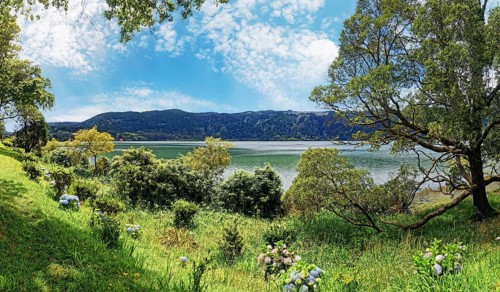 Panoramic view of Furnas Lake surrounded by grass and trees under a clear blue sky, Furnas, Sao