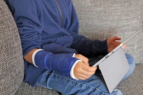 Boy with arm in plaster sits on the sofa with a tablet