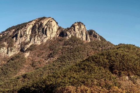 Landscape of tree cover mountain with peak of granite set against clear blue sky in South Korea