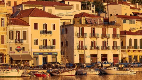 The last rays of sunshine of the day cosily illuminate the waterfront with cafes and boats, Gythio,