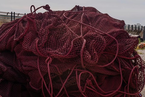 Closeup of large ball of maroon colored fishing nets in front of sea wall on cloudy day in South