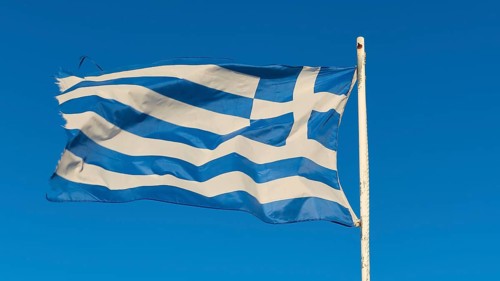 The Greek flag fluttering in the wind on a mast, against a clear blue sky, Gythio, Mani,