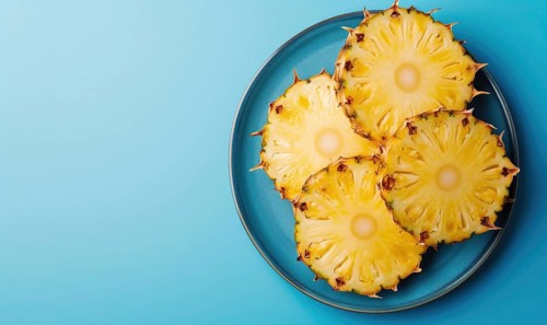 Pineapple slices on blue plate over blue background. Top view with copy space AI generated