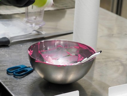 A mixing bowl with remnants of pink icing and a spatula on a kitchen counter