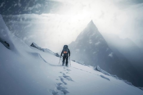 A mountaineer in mountains approaching a majestic snowy mountain peak amidst a snowfall and snow