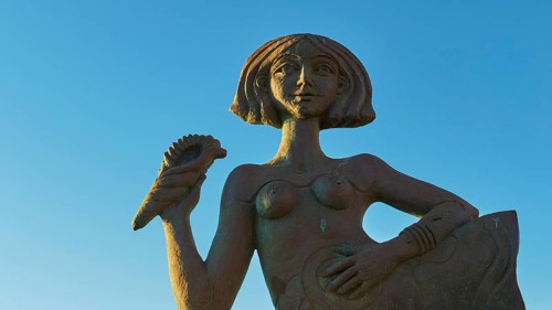 A female statue holding up a palm, mermaid, against a clear blue sky, Gythio, Mani, Peloponnese,