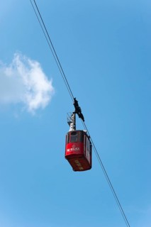 Red cable car gondola hanging on a rope against a clear blue sky with few clouds, Balea Cascada