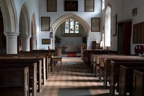 View past wooden pews to chancel arch and altar in sanctuary in the church at Milton Lilbourne,