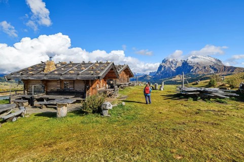 Edelweiss hut on Alpe di Siusi, hiker with red rucksack, Sassopiatto and Sassolungo, clouds,