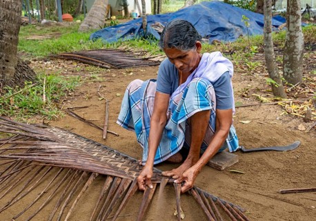 A village woman demonstrates the traditional craft of making mats from coconut leaves using her